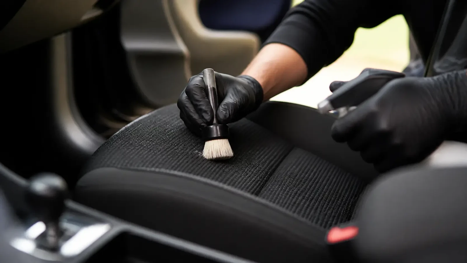 Een vlek op een stoffen autostoel die met een borstel wordt behandeld.